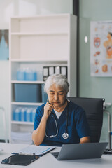 Thoughtful Hispanic female doctor sitting at her desk in a bright medical office, looking at a laptop screen.