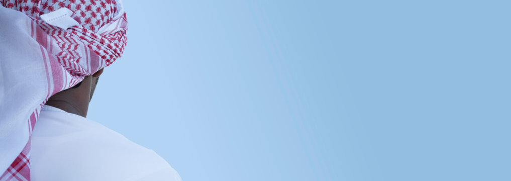 Arab man from behind with a red and white keffiyeh styled as a turban on light blue gradient background with large copy space for text or graphic elements 