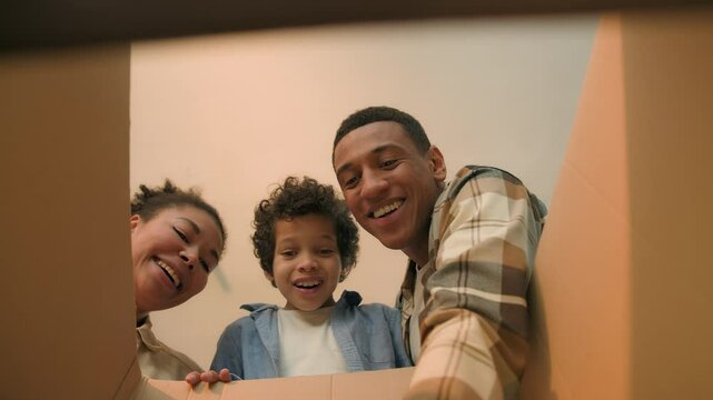 POV point of view inside box African American family parents little boy child open unpacking cardboard parcel happy joyful kid surprise buy teddy bear toy birthday present shopping delivery moving day