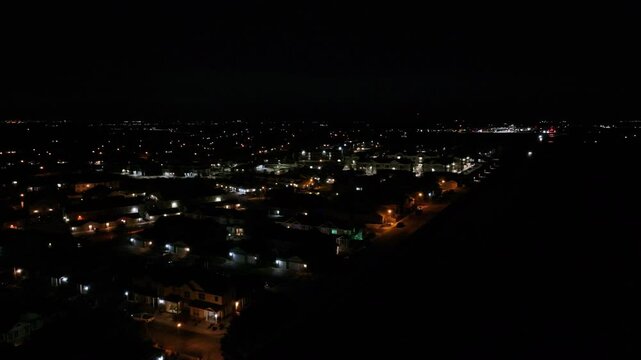 Aerial view of a condominium complex on residential streets at night next to a highway with homes and apartments in the distance.