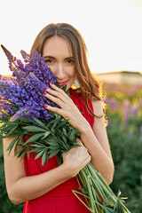 beautiful girl in a red dress with a bouquet of lupine flowers in the field