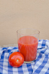 Vertical photography of a appetizing glass of spanish traditional gazpacho or tomato juice along with a ripe tomate from the garden. Healthy organic sustainable food and nutrition. Copy space.