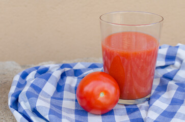 Horizontal close up photography of a appetizing glass of spanish traditional gazpacho or tomato juice along with a ripe tomate from the garden. Healthy organic sustainable food and nutrition.