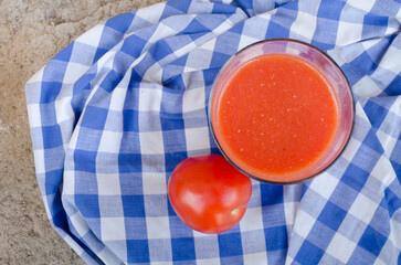 Horizontal top view photography of a traditional summer glass of spanish gazpacho or tomato juice along with a ripe tomate from the garden. Health, nutrition, organic, sustainable food. Copy space.