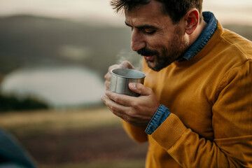 Smiling man enjoying hot tea or coffee outdoors during a morning camping