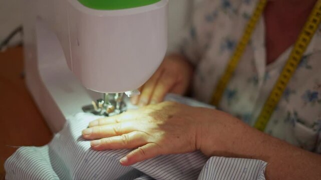 A senior woman skillfully sews blue striped fabric using a white sewing machine. retirement concept