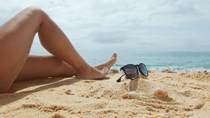 Woman sits on a sandy sea beach on a sunny summer day.  Female legs in the frame.