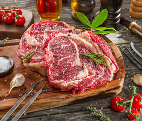 Raw beef steaks with herbs and spices ready for cooking are on wooden board.