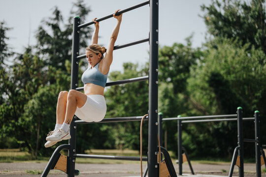 Fit girl exercising abs on parallel bars in the park on a sunny day, demonstrating a healthy lifestyle and outdoor fitness.