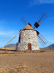 Traditional Fuerteventura windmill under blue sky. Circular windmill with blades in rural landscape. Cultural heritage of the Canary Islands.