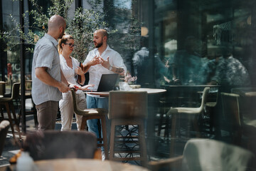 Colleagues engaged in a business meeting in an urban outdoor cafe, discussing project details using a laptop.