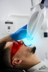 Patient whitens his teeth wearing goggles and lip retractor. Dental whitening procedure by...