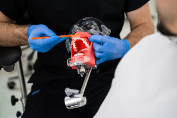 Doctor uses jaw dental model to explain patient technique of brushing teeth. Teeth brushing technique showing by dentist.