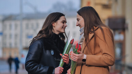 two happy girls, students, friends with flowers in their hands, laughing