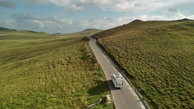 Aerial view of a campervan driving on a road through a beautiful mountain landscape. Drone slow motion shot tracking a motorhome on a highland road in a sunny evening