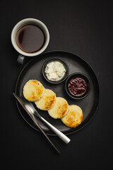 Appetizing breakfast on a black plate on a black background. Black coffee and cottage cheese casserole