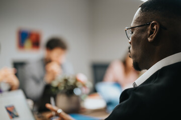 A close-up view of a focused businessman wearing glasses, participating in a meeting with blurred colleagues in the background, working collectively on project ideas and business strategies.