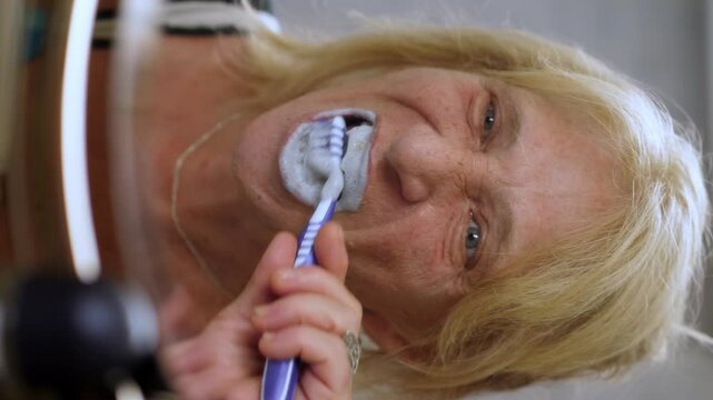 Vertical: A mature woman carefully brushes her teeth in the bathroom, maintaining good oral hygiene.