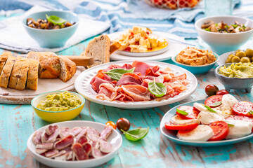 Picnic table with assorted appertizers, raw vegetables, cheese, dips, baguette and pastrami and...