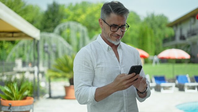 Handsome mature man using smartphone by hotel pool on vacation - Powered by Adobe
