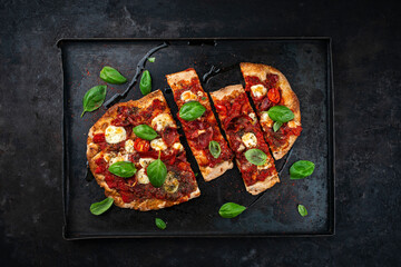 Traditional Italian pensa bread prosciutto e salsa di pomodoro with Parma ham, buffalo mozzarella tomato sauce served as top view on an old rustic tray