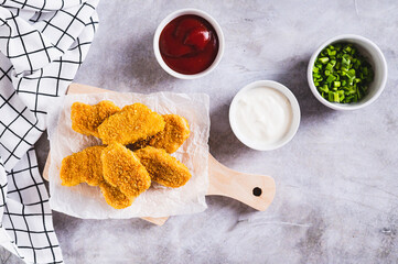 Crispy nuggets on paper on a board and sauce in a bowl on the table top view