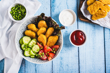 Bowl with crispy nuggets, tomato and cucumber on the table top view
