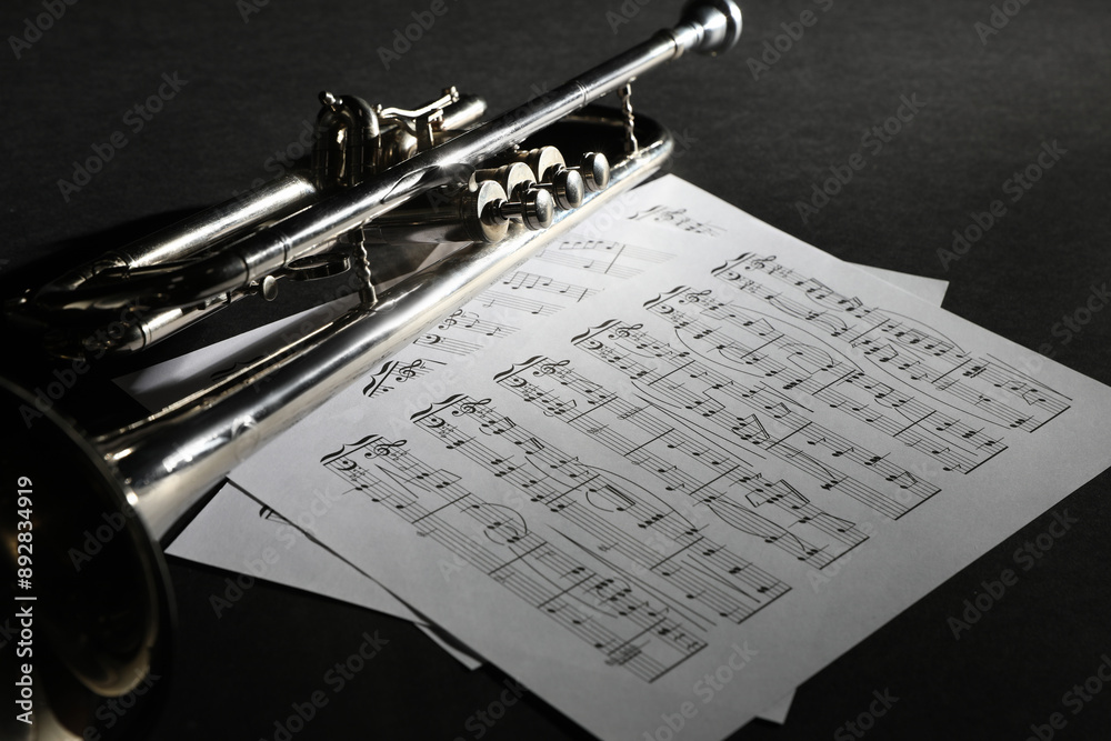 Wall mural Closeup view of shiny trumpet and music sheets on dark background. Wind musical instrument