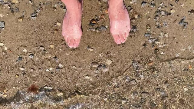 Person's bare feet standing in shallow water with red algae in the sand, slow motion
