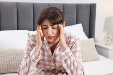 Upset woman suffering from headache on bed at home