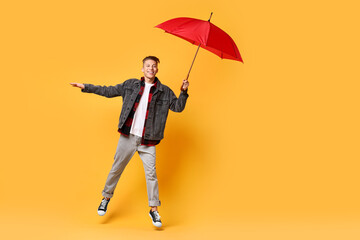 Young man with red umbrella jumping on yellow background, space for text