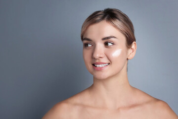 Beautiful woman with cream on her face against gray background