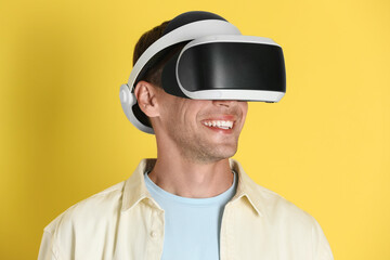 Smiling man using virtual reality headset on yellow background