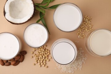 Different types of vegan milk and ingredients on beige table, flat lay