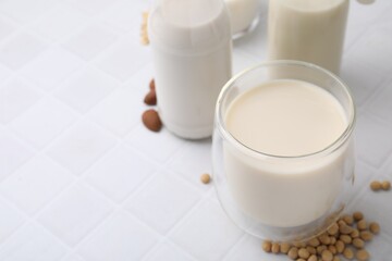 Different types of vegan milk and ingredients on white tiled table, closeup. Space for text