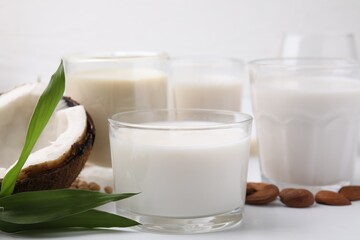 Different types of vegan milk and ingredients on white table, closeup