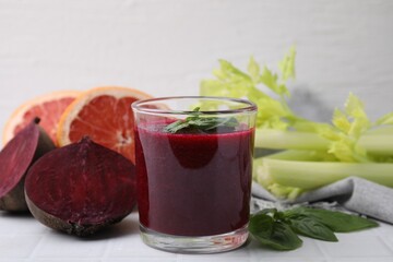 Tasty beetroot smoothie with basil in glass, fresh vegetables and grapefruits on light tiled table, closeup. Vegan drink