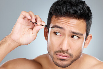 Obraz premium Man, idea and tweezers by eyebrow in studio for grooming, facial epilation and wellness or skincare. Male person, cosmetic tool and thinking of hair removal, gray background and hygiene routine.