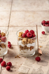 Berry dessert in glass with granola, fresh raspberries, yogurt or cream cheese. Healthy breakfasr concept, on beige tile background with text space