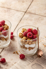 Berry dessert in glass with granola, fresh raspberries, yogurt or cream cheese. Healthy breakfasr concept, on beige tile background with text space