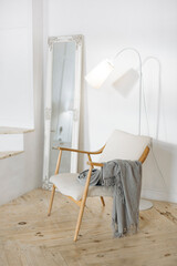 Minimalist space with a cozy chair and gray throw, tall ornate mirror, and a sleek floor lamp. Bright lighting and simple decor create a serene atmosphere