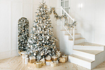 Beautifully adorned Christmas tree with gold and white presents, positioned next to a staircase with festive garlands. The mirror reflects the warm, cozy atmosphere