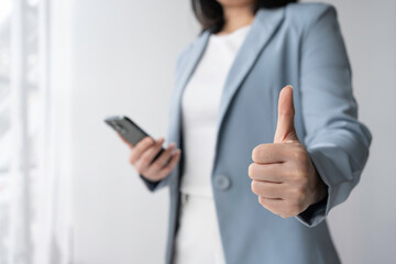A confident professional woman giving a thumbs-up gesture while holding a smartphone, showcasing positivity and success in business.