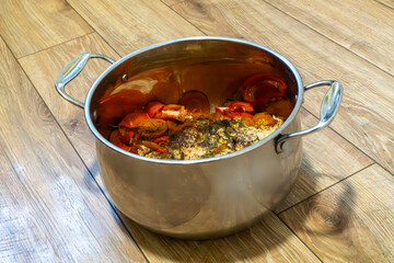 A large stainless steel pot filled with cooked crab and vegetables on a wooden floor, representing homemade seafood cuisine