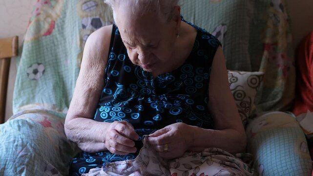 A 90-year-old woman mends a torn sweater, showcasing her skill and patience in repairing clothing. This close-up highlights the meticulous process of mending.