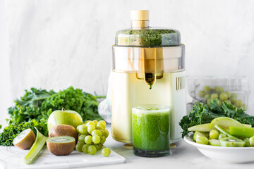 A juicer making a healthy green juice with the ingredients all around.