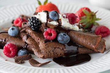 Homemade chocolate crepes topped with whip cream, berries and chocolate sauce.