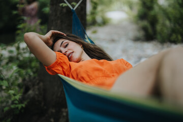 Fototapeta premium Smiling young woman enjoying a peaceful moment in a hammock outdoors. Relaxation and nature combined in a serene setting.