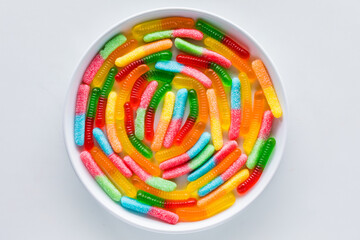 Bright colourful gummy worms in a spiral against a light background.