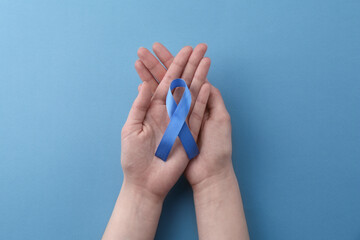 Woman with blue awareness ribbon on color background, top view
